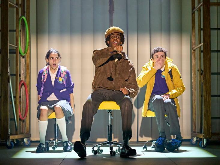 group of actors portraying children  pantomimes driving bus while two other children sit behind