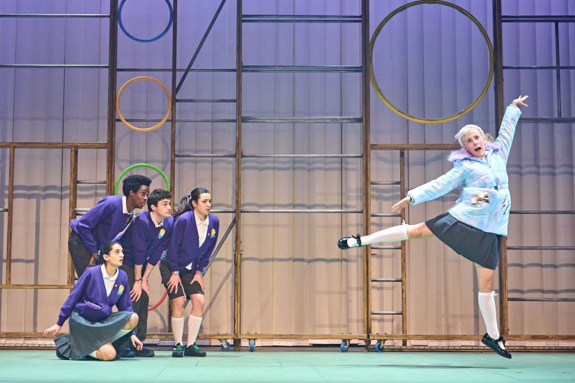 Women dances in ballet while a group of actors portraying children look on.