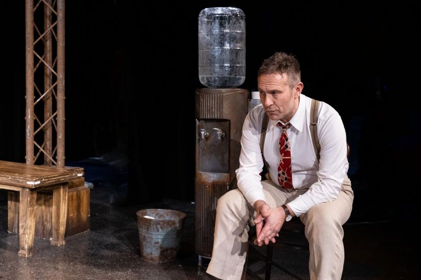 A man in a suit sits on a chair by a water cooler