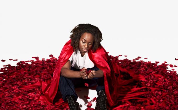 A woman sits on the floor in a red cape, which turns into petals on the floor