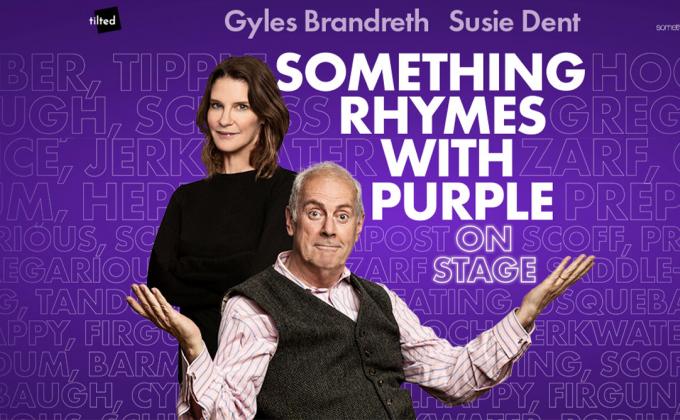 Gyles Brandreth raises his hands in a questioning manner, Susie Dent stands behind