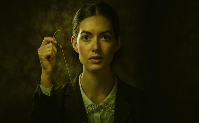 A woman holds a needle and string in her hand