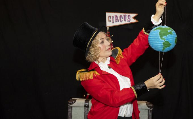 A woman in a red circus jacket and top hat, she is holding a globe