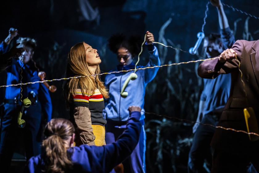 A girl stands surrounded by people pulling telephone wires