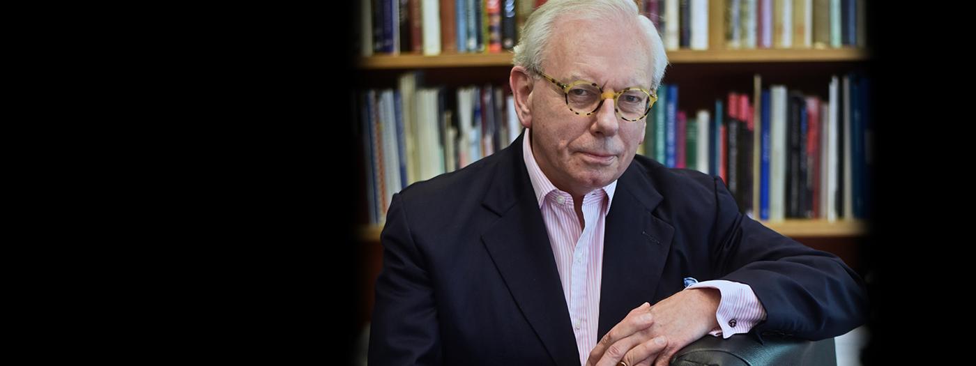 David Starkey sitting with arms crossed by books