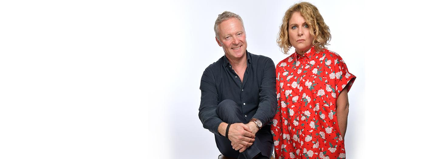 Rory Bremner laughs, sitting on chair, with Jan Ravens in a red dress looking a bit more serious