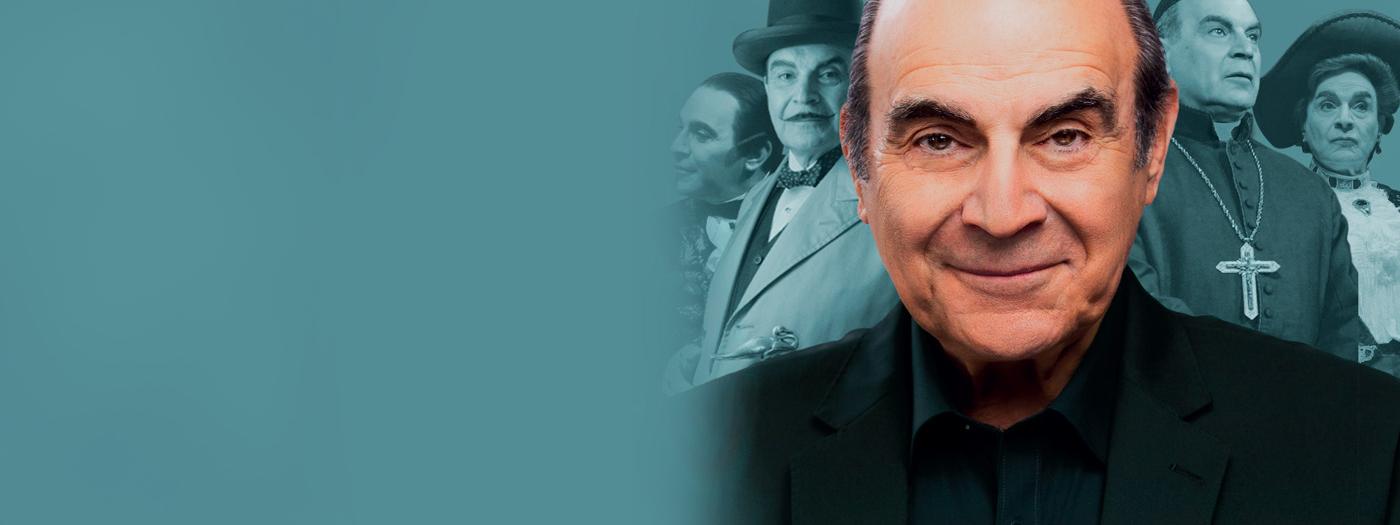 David Suchet in a black suit, behind him are photographs of previous performances he has played