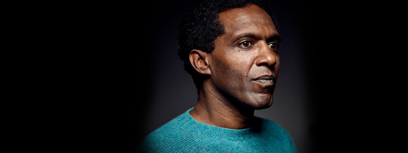 Lemn Sissay portrait photograph, he wears a turquoise blue jumper. 